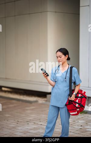 Healthcare worker using smartphone carrying medical bag outdoors Stock Photo