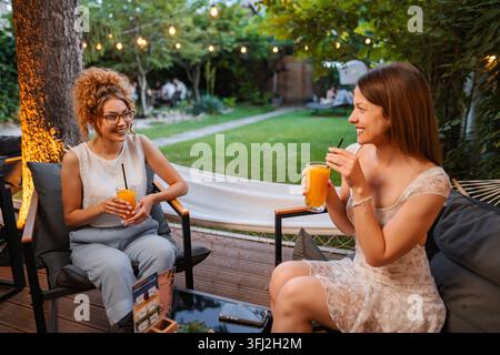 Two women friends relaxing, drinking orange juice in garden cafe Stock Photo