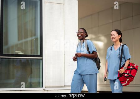 Diverse medical students laughing, walking outside hospital Stock Photo