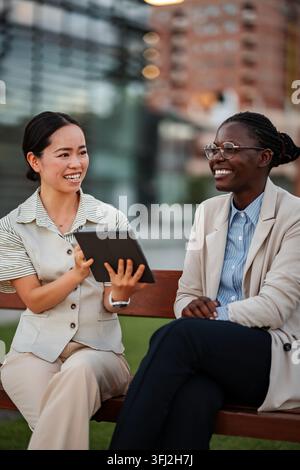 Diverse businesswomen collaborating with tablet during outdoor meeting Stock Photo