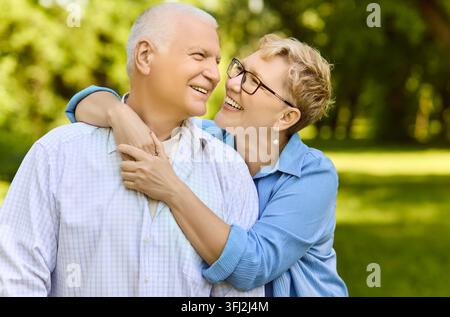 Happy senior couple hugging in sunny park, smiling with love and joy outdoors Stock Photo