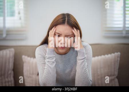 Stressed Asian woman holding head on sofa suffering from headache or migraine Stock Photo