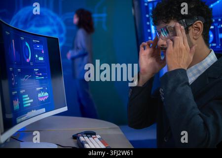 Business executive wearing smart glasses analyzing digital dashboards and business intelligence metrics in a modern office, demonstrating AI powered a Stock Photo