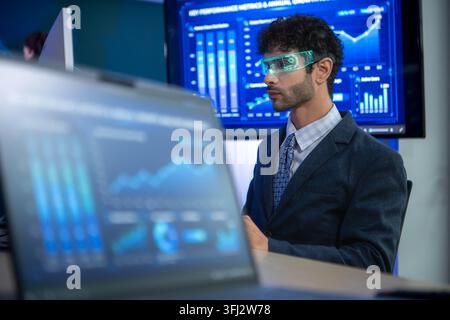 Business executive wearing smart glasses analyzing digital dashboards and business intelligence metrics in a modern office, demonstrating AI powered a Stock Photo