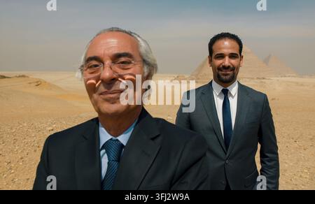 Two confident Egyptian businessmen in dark suits standing proudly near the iconic Giza pyramids in the desert ideal for Middle E Stock Photo