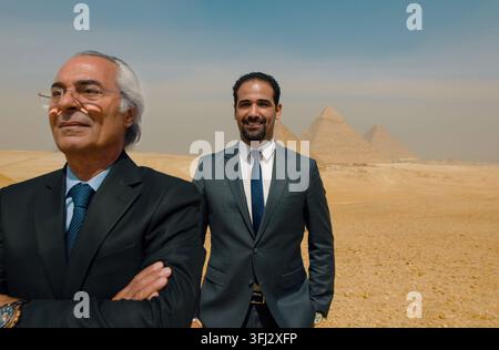 Two confident Egyptian businessmen one senior and one younger in formal suits standing before the Giza pyramids in bright desert Stock Photo