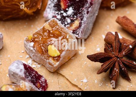 Assorted Turkish delight cubes with pistachios and powdered sugar on craft paper, decorated with star anise and cinnamon sticks. Traditional oriental Stock Photo