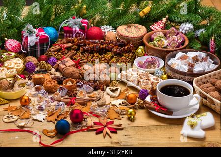 Wide angle festive display of assorted Turkish sweets, nuts, and coffee surrounded by Christmas pine branches, gift boxes, and colorful ornaments Stock Photo