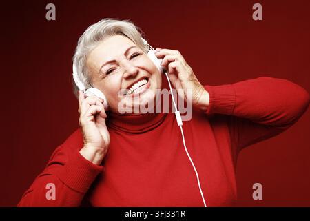 Close up photo of happy senior caucasian woman with headphones isolated over red background Stock Photo