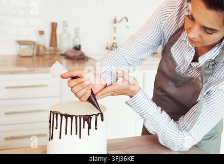 Pastry female chef in the kitchen decorating a cake of chocolate. Stock Photo