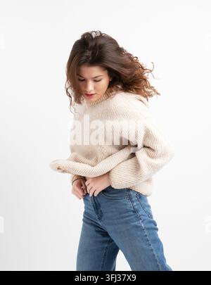 Young curly woman with long hair in a sweater and blue jeans posing over white background. Stock Photo