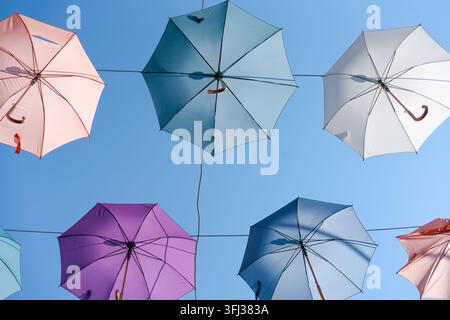 Colorful Open Umbrellas Hang from Cables Against Clear Blue Sky Banner Stock Photo