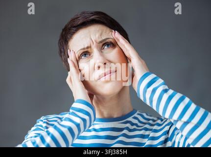 Woman wearing striped shirt with a headache holding head Stock Photo