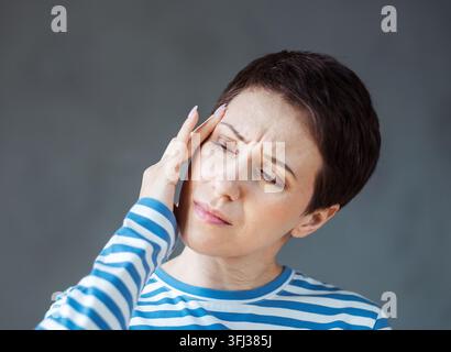 Woman wearing striped shirt with a headache holding head Stock Photo