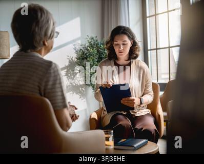 Thoughtful counselor attentively listening and taking notes during an emotional therapy session with an elderly client. The serene office environment, Stock Photo