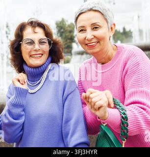Two happy cheerful pensioner female friends in bright sweaters and sunglasses walk together. Stock Photo