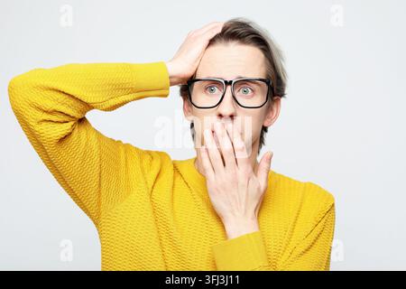 The man in the yellow sweater is surprised and covers his mouth with his palm in amazement. Stock Photo