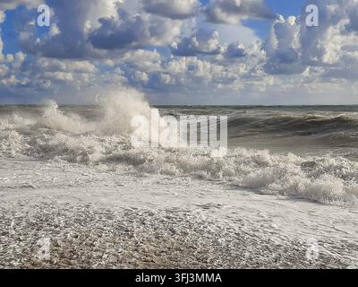 Stormy ocean waves breaking on a pebble beach under a cloudy sky Stock Photo