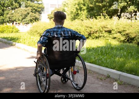 Young disabled man in wheelchair walking park and listening music Stock Photo