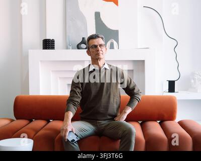Elderly stylish man sitting on a red sofa in a modern room. Stock Photo