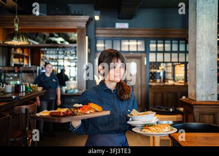 Waitress serving multiple food plates in restaurant Stock Photo