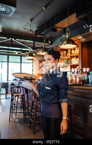 Young adult waitress working in a bar, holding a tray Stock Photo