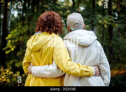 Two old female friends hiking together through the forest in autumn. Back view. Stock Photo