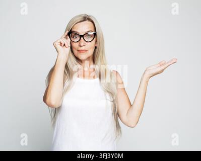 Smile senior woman wearing yellow sweater holding something on open palm Stock Photo