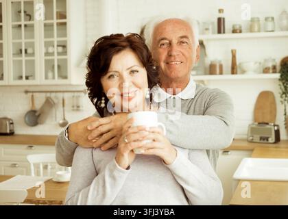 Happy elderly couple hugging in the kitchen at home. Stock Photo