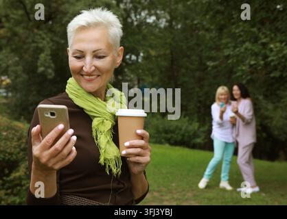 Beautiful old blond woman laughing, holding a cup of coffee to go, take selfie and feeling so happy. Stock Photo