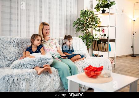 Mother and daughters relaxing on sofa watching TV at home Stock Photo