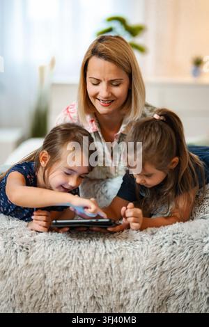 Happy mother and children playing or learning on a digital tablet at home Stock Photo