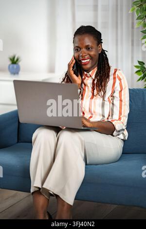 Adult black woman telecommuting working from home on couch Stock Photo