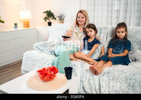 Mother and daughters watching TV relaxing together on couch Stock Photo