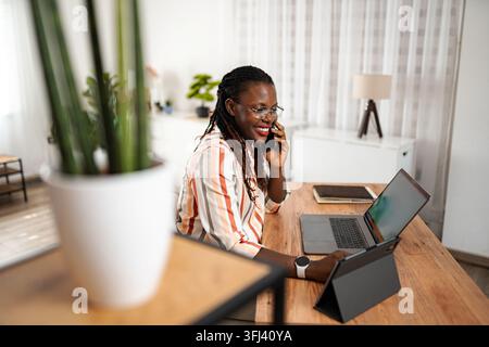 Smiling black woman talking on phone working from home Stock Photo
