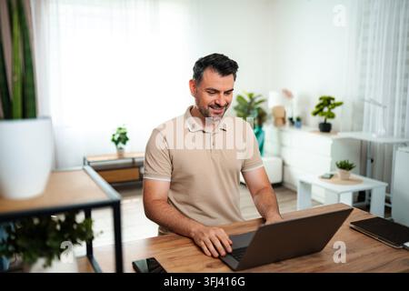 Smiling man working on laptop from home office Stock Photo