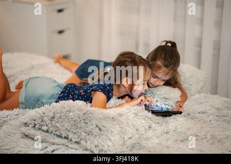 Two preschool age sisters relaxing in bed, sharing a digital tablet Stock Photo