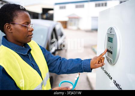 Woman in safety vest charging electric car at self-service station Stock Photo