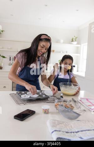 African American mother and daughter wearing denim aprons mixing cupcake batter in bright kitchen. Baking, home, family, mom, te Stock Photo