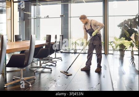 Professional janitor mopping office floor in uniform, corporate cleaning scene Stock Photo