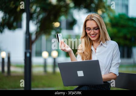 Happy woman making online payment with credit card outdoors Stock Photo