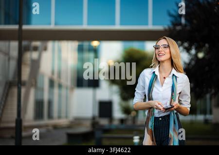 Young businesswoman smiling walking outside modern office building Stock Photo