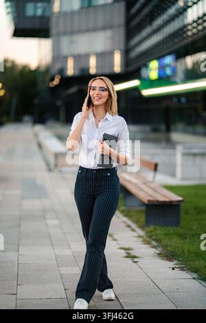 Successful businesswoman talking on smartphone walking in city Stock Photo