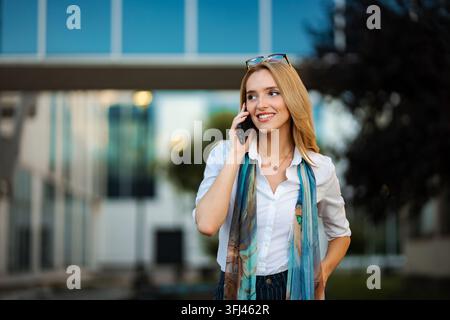 Young businesswoman talking on smartphone and smiling outdoors Stock Photo