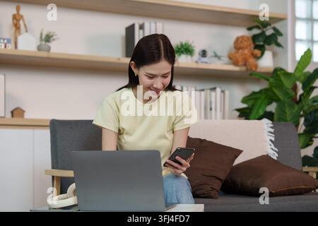 Asian woman using smartphone and laptop at home for remote work and digital AI technology Stock Photo