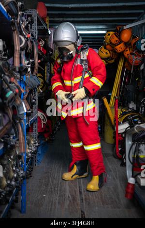 Firefighter wearing protective clothing and breathing equipment prepares a helmet inside an emergency rescue equipment storage area Stock Photo