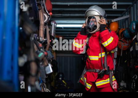 Firefighter wearing protective clothing and breathing equipment prepares a helmet inside an emergency rescue equipment storage area Stock Photo