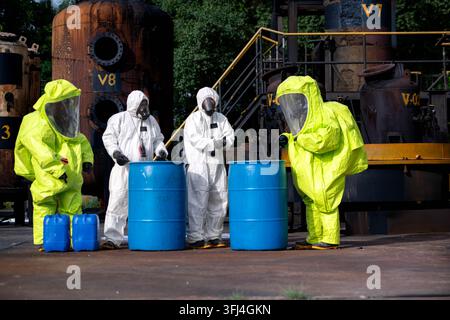 Four workers in chemical protective suits handle blue barrels during hazardous material emergency training Stock Photo