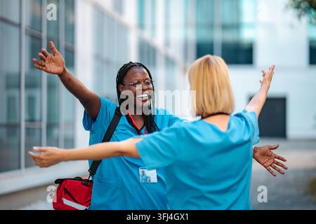 Two smiling women healthcare workers embracing outdoors in scrubs, showing friendship and happiness Stock Photo