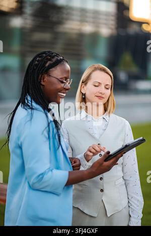 Diverse businesswomen collaborating using digital tablet outdoors in office park Stock Photo